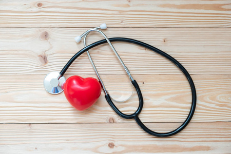 听诊器，木制背景上有红色心形。 医疗及保险概念