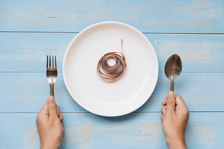 顶部的女人手拿勺子和叉子上面的白色盘子,粉红色的测量带在蓝色的