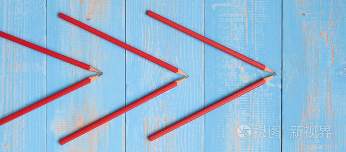 蓝色木制背景上箭头形状的红色铅笔。 跟进前进战略团队合作和商业成功理念。 顶部视图和复制空间