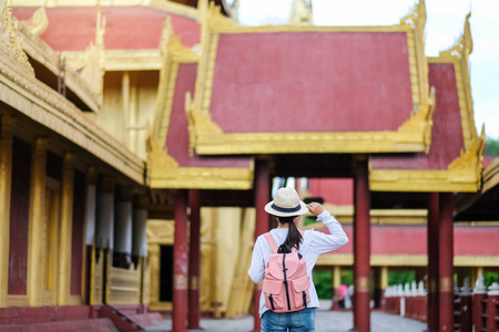 女旅行背包客戴着帽子，亚洲旅行者站在曼德勒宫，是缅甸最后一个君主制的最后一个皇宫。 缅甸旅游景点的地标和热门景点