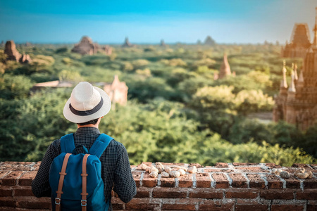 年轻人旅行背包客，戴着帽子，亚洲旅行者站在宝塔上，看上去美丽的古寺庙，地标性建筑，在巴甘缅甸的旅游景点很受欢迎。 亚洲旅游概念