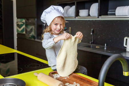 小女孩带着厨师帽，擀面杖，准备面团，在厨房里烤自制的节日苹果派。 孩子在家做健康的食物，玩得开心。 儿童家庭团队帮助概念