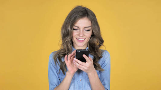 年轻女孩浏览智能手机，与黄色背景隔离
