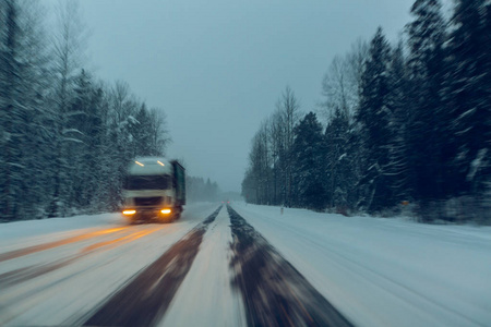 在暮色中, 当雪飞来的时候, 卡车在冬天的路上开着大灯行驶。在危险的条件下驾驶的概念, 冬季能见度差。图片与莫蒂