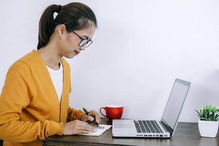 快乐休闲的年轻亚洲妇女在家里或小办公室工作，使用笔记本电脑和文件报告在办公桌上作为自由职业者。