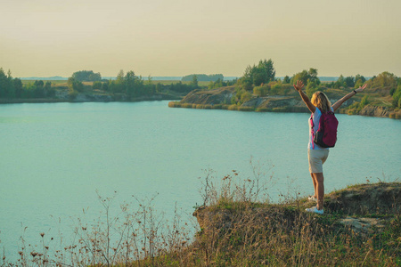 年轻女子带着粉红色的背包站在蓝色白垩采石场的背景上，背景在日落的时候很近