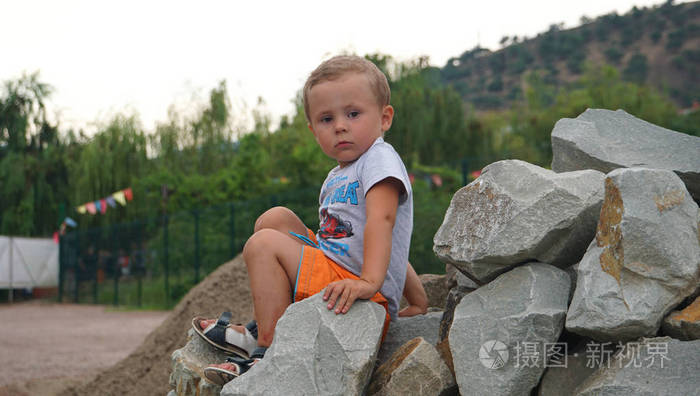 那个穿橙色短裤坐在石头上的小男孩在海洋海岸的其余部分中的自然活动