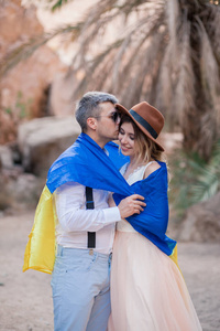裹着乌克兰国旗的年轻夫妇在峡谷里亲吻棕榈树和岩石的背景。 特写镜头。