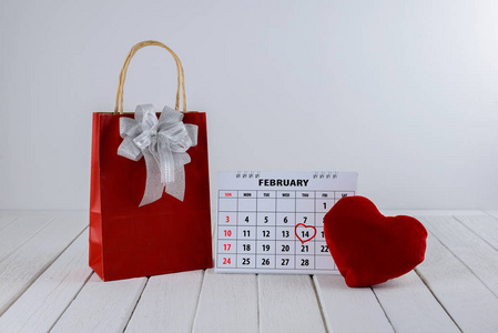 日历页红手写心突出2月14日圣瓦伦日与红色礼品袋和心形在白色木桌上