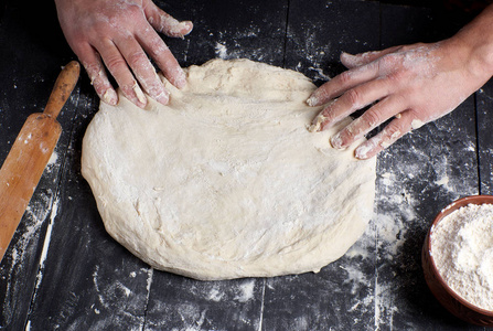 s hands knead a round piece of dough for making pizza, top view