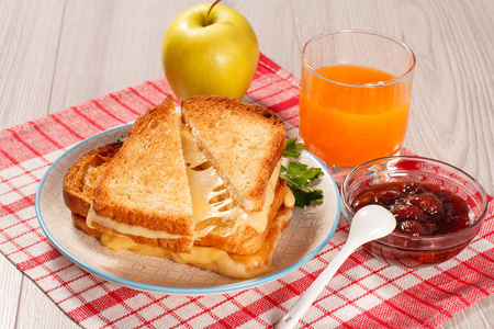 烤面包片，奶酪和绿色欧芹在白色盘子玻璃橙汁苹果和玻璃碗草莓果酱在红色厨房餐巾纸。 早餐的好食物。