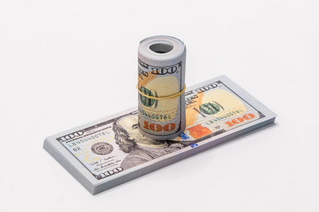 一堆面值100美元的美元卷起, 与一个简单的橡皮筋放在一起, 一叠100美元纸币, 在白色的背景下被隔离