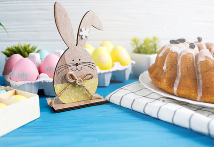 复活节快乐手工制作的蛋糕在毛巾上，鸡蛋，木制兔子兔子在蓝色的木制背景上。复活节装饰