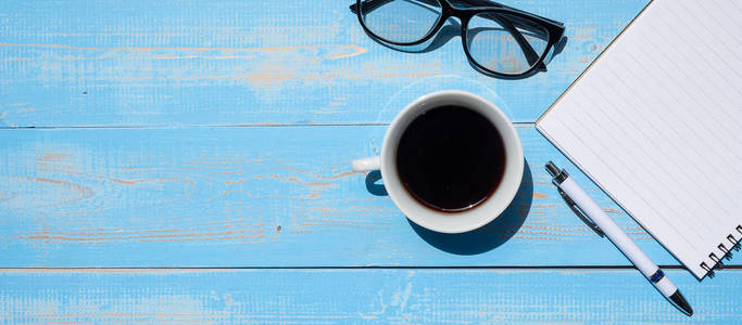  pen, notebook and eyes glasses on blue wooden table background.