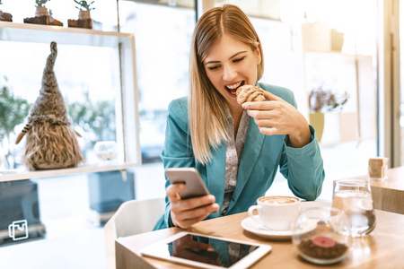 年轻的微笑女商人用智能手机在咖啡馆休息