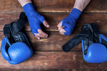 s hands in boxing bandages and boxing gloves on a wooden backgro