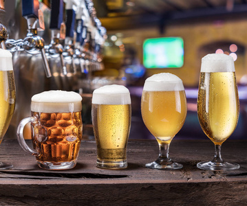 旧木桌上放着冰镇杯子和啤酒杯。 酒吧内部和酒吧柜台与啤酒水龙头的背景。 各种啤酒。