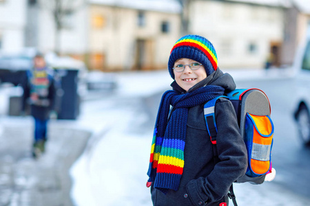 两个小学生在下雪的时候步行去学校。快乐的孩子玩第一次雪。兄弟姐妹与背包在五颜六色的冬天衣裳的朋友