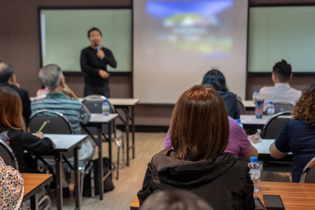 观众的后侧听着，亚洲演讲者穿着休闲服在舞台前的会议室里，会议室里的商业和教育理念