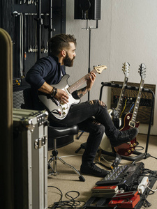 一个留着胡子的男人在录音室里坐着弹电吉他的照片。