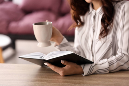 美丽的年轻女子一边喝咖啡一边在家看书