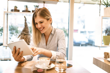 年轻的微笑女商人用平板电脑在咖啡馆休息