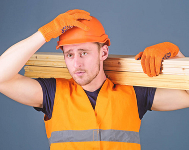 木匠, 木工, 强的建设者在严肃的面孔运载木横梁在肩膀上。安全和保护概念。男子头盔, 硬帽子和防护手套持有木梁, 灰色背景