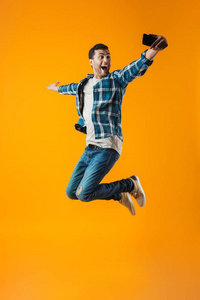 一个穿格子衬衫的快乐年轻人的全长肖像，被隔离在橙色背景下跳跃，自拍