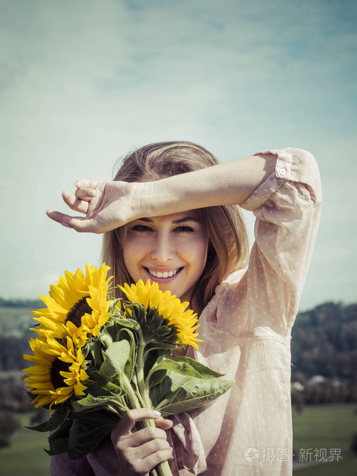 一个快乐的年轻女人在阳光下抱向日葵的照片
