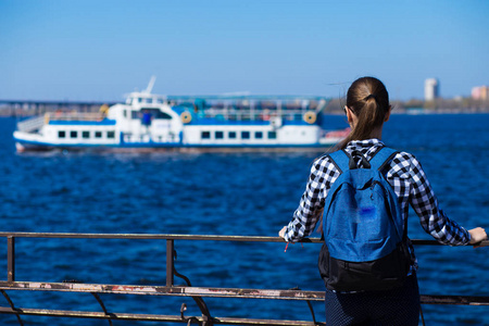 阳光明媚的春天，背着背包站在海边的码头上的旅游妇女的后景