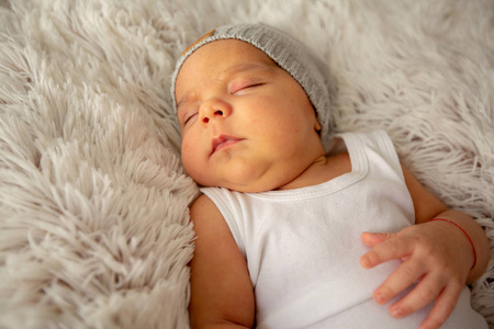 一个漂亮的男婴，一个婴儿，睡在帽子上，睡在蓬松的毯子上
