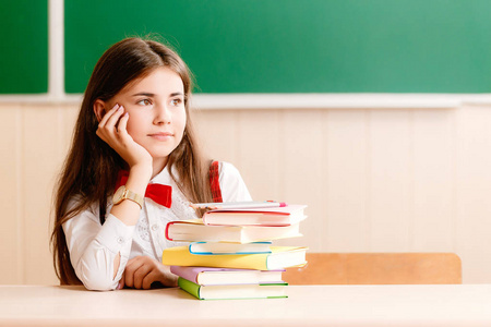 可爱的黑发女学生坐在学校的桌子上,黑板上有书.照片