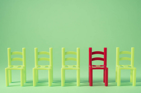 独特的红色椅子排着绿色的其他。 领导观念。 靠墙的空椅子。 独特性与他人区别的概念。