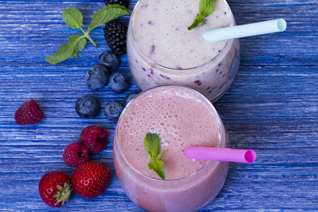 覆盆子草莓蓝莓冰沙在蓝色木制背景上。 带新鲜浆果的奶昔。 健康的早餐。 水果奶昔和配料。 幸福和重量松散的概念。 顶部视图