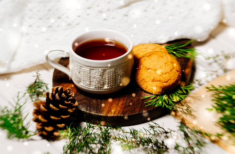 白色茶杯和饼干的背景针织格子和木制桌子。 冬天早晨的浪漫早餐