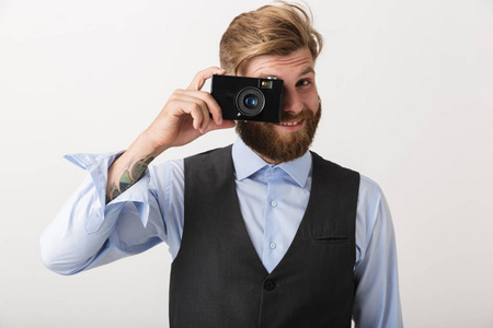 一位英俊的年轻胡须男摄影师站在白色墙壁背景上，手持相机。