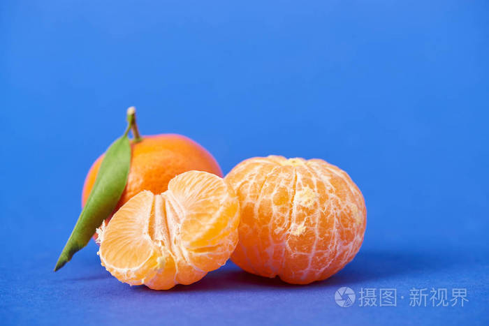 在蓝色背景上半个剥皮的橘子靠近整个柠檬