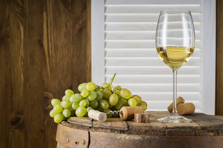 仍然生活的白酒与木制桶与复制空间。 酒瓶，一杯白葡萄酒和一串葡萄在一个旧的木桶上。 品酒和生产理念。