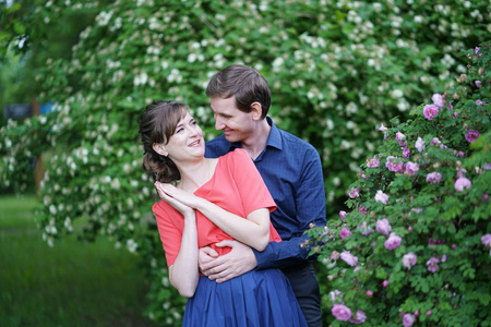 一对善良的成年夫妇走在绿色的夏日花园里，拥抱微笑，亲吻爱情