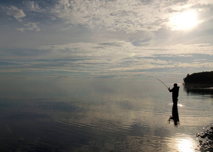 日落时渔夫的剪影。在湖上钓鱼