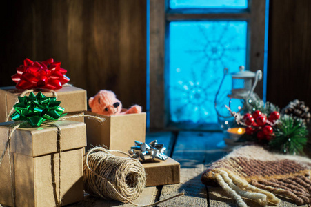 圣诞礼物放在旧木桌上，背景是老式的白雪覆盖的窗户。 乡村圣诞装饰。 包装礼物。