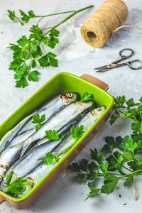 在浅灰色混凝土台面上用欧芹抹在绿色盘子上的沙丁鱼或波罗的海鲱鱼。生的未煮熟的海鱼。