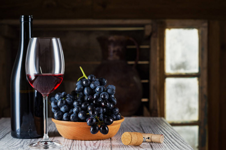 木桶红酒的静物。酒瓶，一杯红酒和一个旧木桶上的葡萄..品酒和生产理念..