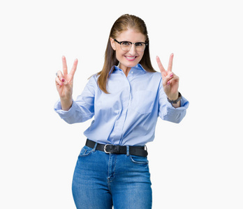 漂亮的中年成熟商务女性戴着眼镜，在孤立的背景下微笑着看着镜头，露出手指在做胜利的标志。第二名。