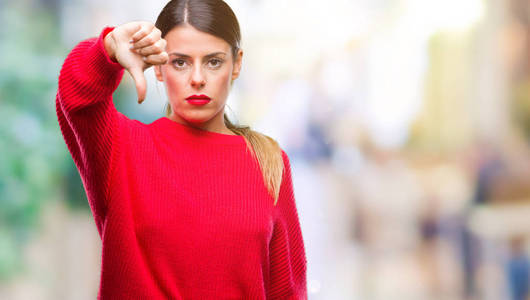 年轻漂亮的女商人穿着冬天的毛衣，在孤立的背景上看起来不高兴和愤怒，表现出拒绝和消极的拇指向下的手势。 不好的表情。