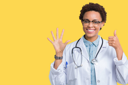 年轻的非裔美国医生女士穿着医用外套，在孤立的背景上显示和举着手指第六，同时微笑自信和快乐。