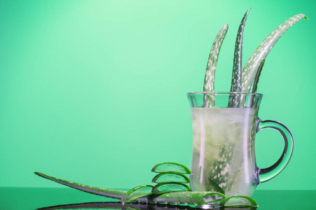 芦荟仙人掌的叶子在玻璃杯里。 芦荟汁在玻璃上的绿色背景与文字空间。 健康饮料芦荟与复制空间。