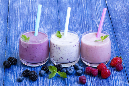 蓝木背景上的覆盆子草莓和蓝莓冰沙。 带新鲜浆果的奶昔。 浆果酸奶与蓝莓，覆盆子和黑莓。 夏季健康素食早餐。