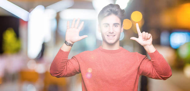 年轻的英俊男子在孤立的背景显示和指向7号手指，同时微笑自信和快乐。