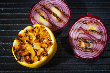 烤洋葱和柠檬特写。 美味的食物背景。 烤架上有条纹的蔬菜。 把烤菜放在平底锅里